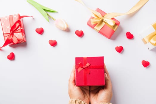 Valentine's day and birthday. Woman hands holding gift or present box decorated and red heart surprise on white background, Female's hand hold gift box package in craft paper Top view flat lay