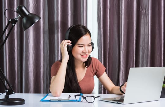 Work from home, Asian young businesswoman smile wearing headphones video conference call or facetime by laptop computer meeting with team on desk at home office