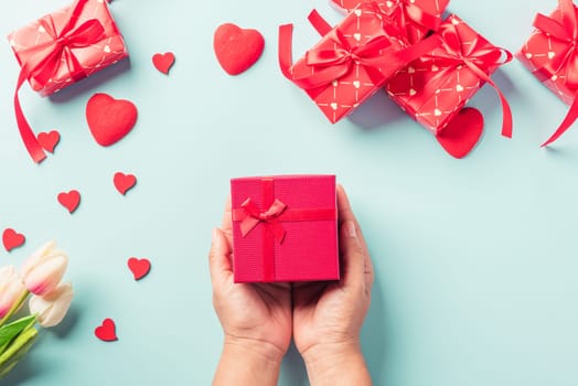 Valentine's day and birthday. Woman hands holding gift or present box decorated and red heart surprise on blue background, Female's hand hold gift box package in craft paper Top view flat lay