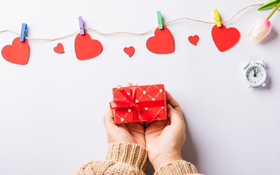 Valentine's day and birthday. Woman hands holding gift or present box decorated and red heart surprise on white background, Female's hand hold gift box package in craft paper Top view flat lay