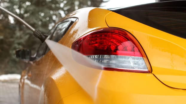 Yellow car back washed at self serve carwash, jet water stream spraying on rear light