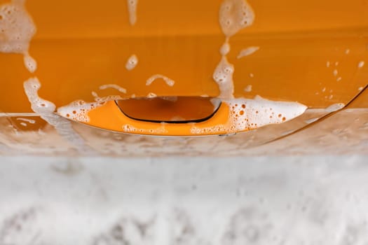 Yellow car door handle covered with shampoo and foam when washed in carwash.