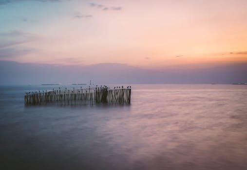 long exposure wooden pole in sea at dusk. Pastel blue and pink sky in Bangpu Thailand