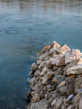 Stone wall on the water, serves as protection. Large stones stacked on top of each other.