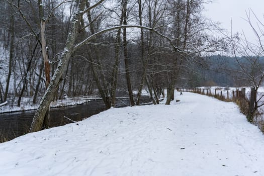Snow-covered path along a narrow river in winter.