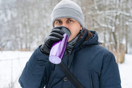 A man drinks from a purple thermos on a winter walk.