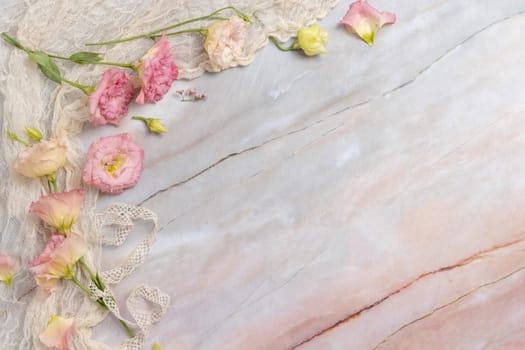 Pink flowers with vintage ribbons and fabric on marble table with copy space, top view