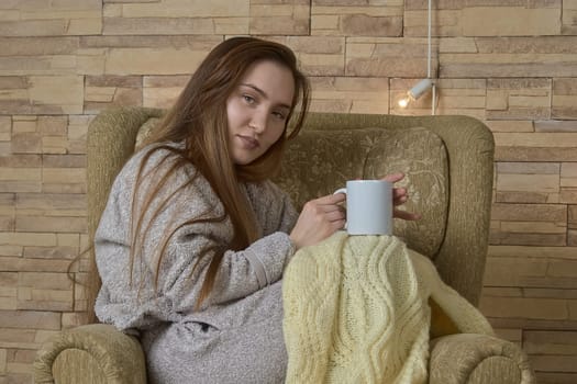 A girl with a cup of tea in her hands is resting in a chair. High quality photo