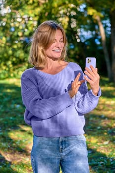 A woman in a park in the summer speaks during a video call on the phone. High quality photo