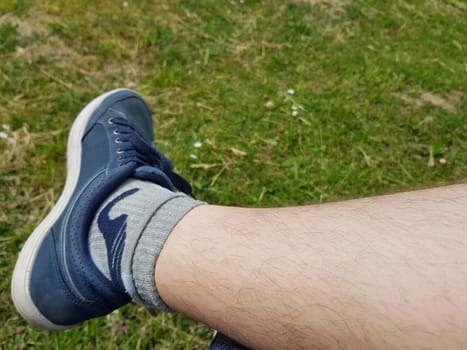 A man's foot with a blue shoe in a background of grass