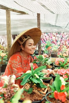 Asian woman with Vietnamese straw hat is smiling and holding potted flower in the garden. Small business concept. Colorful potted flowers Euforbia Spurges bring lucky energy at your home.