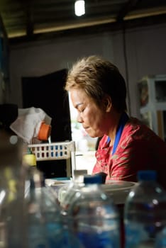 Thai woman washing dishes in the kitchen behind of unfocused glass bottles. Portrait of asian woman working in the kitchen in Thailand.