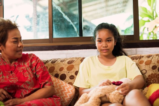 Happy mother talking with her daughter by sitting on couch at home in Thailand. Beautiful asian family and mothers day concept. Asian family full of love and care.