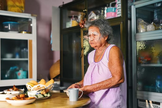Asian old grandmother plating freshly cooked traditional Thai food and set up table in rustic kitchen at home. Family dinner preparation concept.