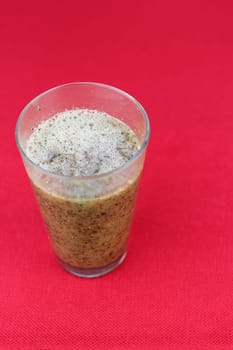 Close-up of blended papaya seeds, pulp and water in a drinking glass close-up on a red place mat. Pureed blend of fresh papaya seeds, papaya pulp and water in a drinking glass on a red background.