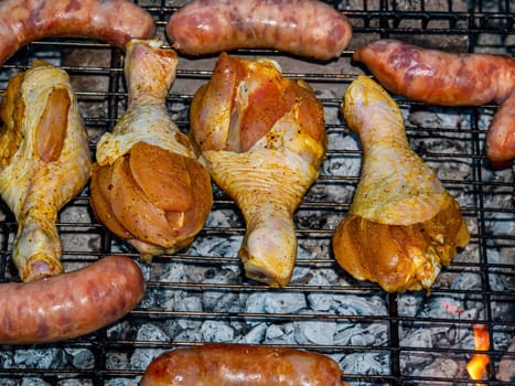 Chicken legs and meat sausages on an iron grill mesh. Cooking over a fire. Grill mesh. Chicken and meat sausages. Healthy eating. Food in nature. Menu of dishes. Background image.