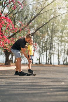 Father holding and training his little son to ride a skateboard in park on spring time. Concept of leisure and outdor family activity. Caucasian man taking care and supporting his kid outdoor.