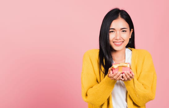 Portrait of happy beautiful Asian young woman smiling holding small gift box on hands, studio shot isolated on pink background, Birthday, New year, Christmas, valentine, holiday day concept