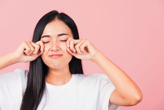 Asian portrait beautiful cute young woman bad mood her cry wipe tears with fingers, studio shot isolated on pink background, Thai female feeling sad unhappy crying with copy space