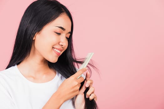 Portrait of Asian beautiful young woman smile combing her hair, happy female long healthy hair with hairbrush brushing hairs, studio shot isolated on pink background