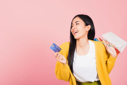 Portrait Asian happy beautiful young woman shopper smiling standing excited holding online shopping bags colorful and credit card for payment on hand in summer, studio shot isolated on pink background
