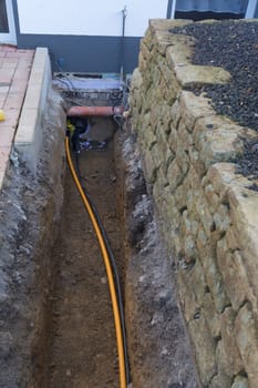 Work on the installation of engineering and heating systems. Two plastic pipes one yellow for gas pipe and one black for power lines. They are in a sand ditch.