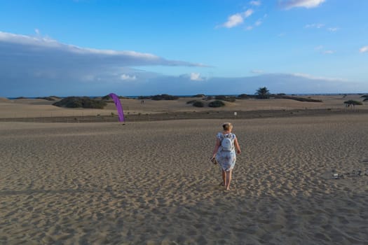 Woman in dress walking in the sand of desert dunes with steps in the desert sand, young woman walking in white sand on a bright summer day, holiday vacation concept