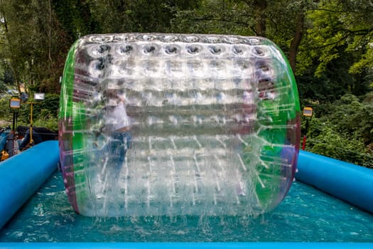 Water or aqua zorbing. Children play inside the inflatable transparent roller floating in swimming pool. Water walking or zorbing very popular fun activity and suitable for all ages.
