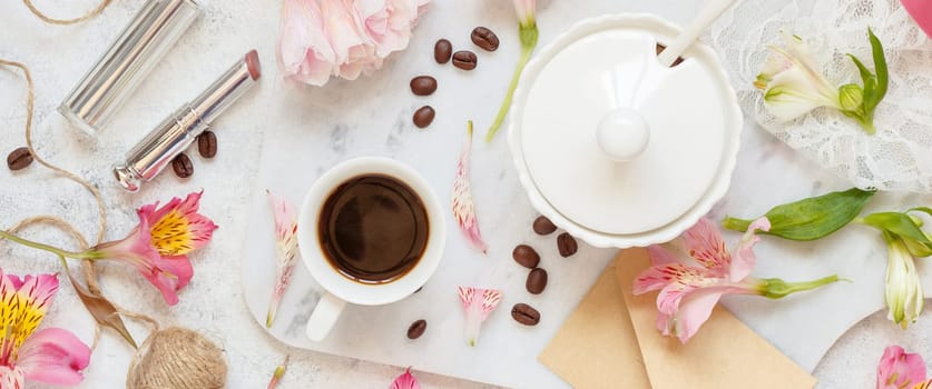 Coffee cup near pink flowers, lipstick and envelope on white table top view. Romantic breakfast