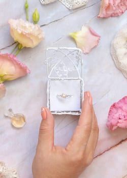 Woman hand opens a gift box with a pearl ring with light pink flowers and vintage ribbons around top view