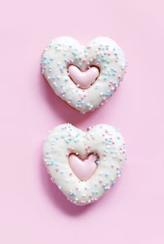 Flat lay of two heart shaped gingerbread cookies with sprinkles and icing on pink background. Top view of tasty Valentine's Day bakery, homemade bakery for romantic holiday