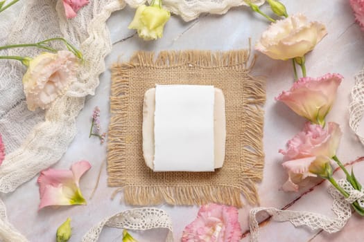 Soap bar on laying on a marble table with pink flowers, petals and vintage ribbons, top view. Soap mockup