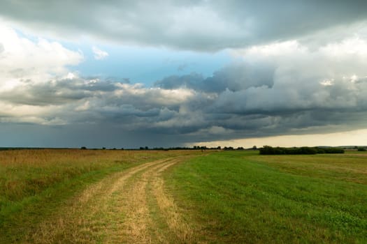 Rural road through meadow and rainy cloud on sky, Czulczyce, Lubelskie, Poland