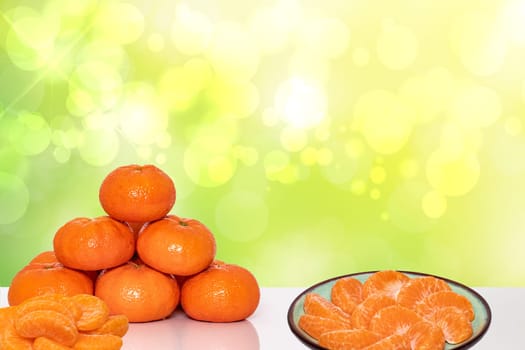 A pile of fresh ripe mandarines, citrus tangerines or orangen and slices of peeled tangerine on a plate over abstract bright background. Space for advertising. Clementines for health nutrition.