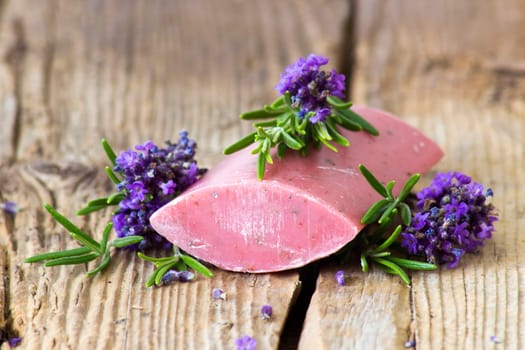 bar of natural soap, lavender flowers and rosemary on old wooden background