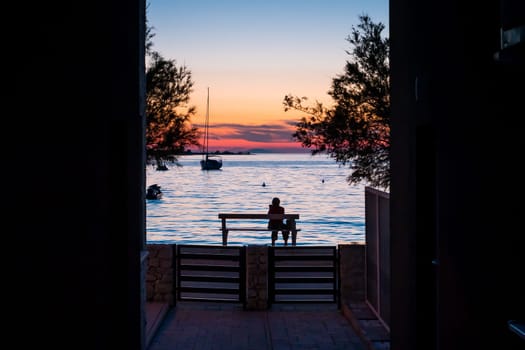A woman sitting on a bench by the sea at sunset and watching the sea and sunset.
