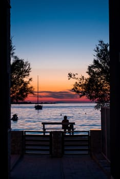 A woman sitting on a bench by the sea at sunset and watching the sea and sunset.
