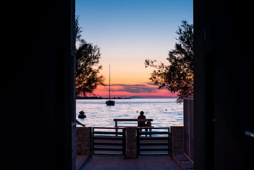 A woman sitting on a bench by the sea at sunset and watching the sea and sunset.