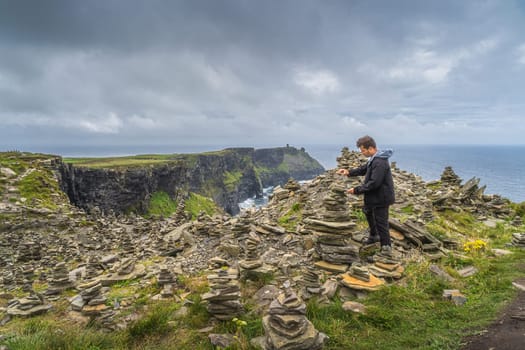 Man, adult stone stacking or rock balancing in iconic Cliffs of Moher, popular tourist attraction, Wild Atlantic Way, County Clare, Ireland