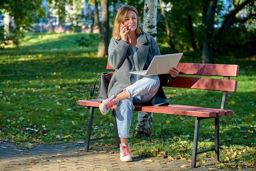A woman with a laptop is sitting on a park bench on a sunny summer day. High quality photo