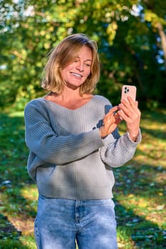 A woman in a park in the summer speaks during a video call on the phone. High quality photo