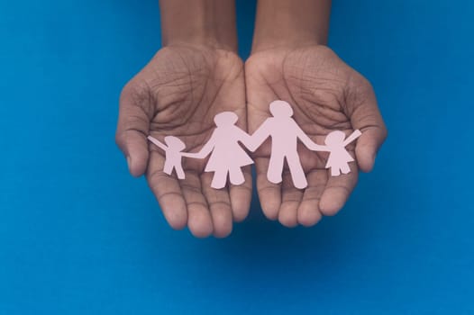 Hand holding family figure cutout top view. World health day Protection against domestic violence, healthcare and medical background. Foster care, homeless support and social distancing concept.