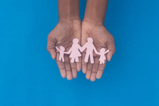 Hand holding family figure cutout top view. World health day Protection against domestic violence, healthcare and medical background. Foster care, homeless support and social distancing concept.