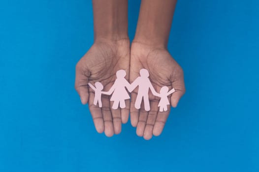 Hand holding family figure cutout top view. World health day Protection against domestic violence, healthcare and medical background. Foster care, homeless support and social distancing concept.