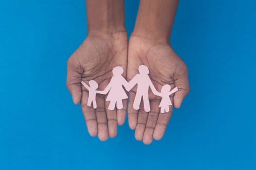 Hand holding family figure cutout top view. World health day Protection against domestic violence, healthcare and medical background. Foster care, homeless support and social distancing concept.