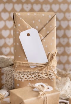 Valentines kraft paper wrapped present with vertical gift tag and hearts close up. Spring scene with blank label. Rustic, cottage chic or bohemian mockup, copy space
