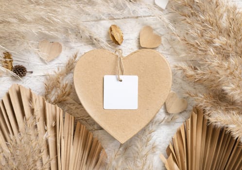 Heart shaped Valentines present with square blank gift tag near dried pampas grass, palm leaves and hearts top view. Rustic, cottage chic or bohemian label mockup, copy space