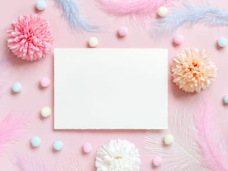 Blank card between pastel flowers, pom-poms and feathers near ring in a gift box on pink top view. Romantic scene with horizontal paper card with place for text flat lay. Valentines, Spring or girlish concept