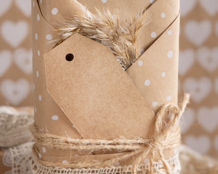 Valentines kraft paper wrapped present with vertical gift tag, hearts and pampas grass close up. Spring scene with blank label. Rustic, cottage chic or bohemian mockup, copy space