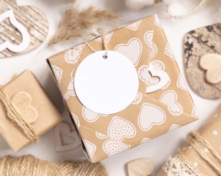 Valentines kraft paper wrapped present with round gift tag near hearts and pampas grass top view. Spring scene with blank label. Rustic, cottage chic or bohemian mockup, copy space